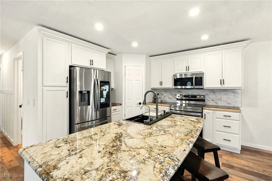 Kitchen featuring dark wood finished floors, appliances with stainless steel finishes, a kitchen bar, a textured ceiling, and a center island with sink