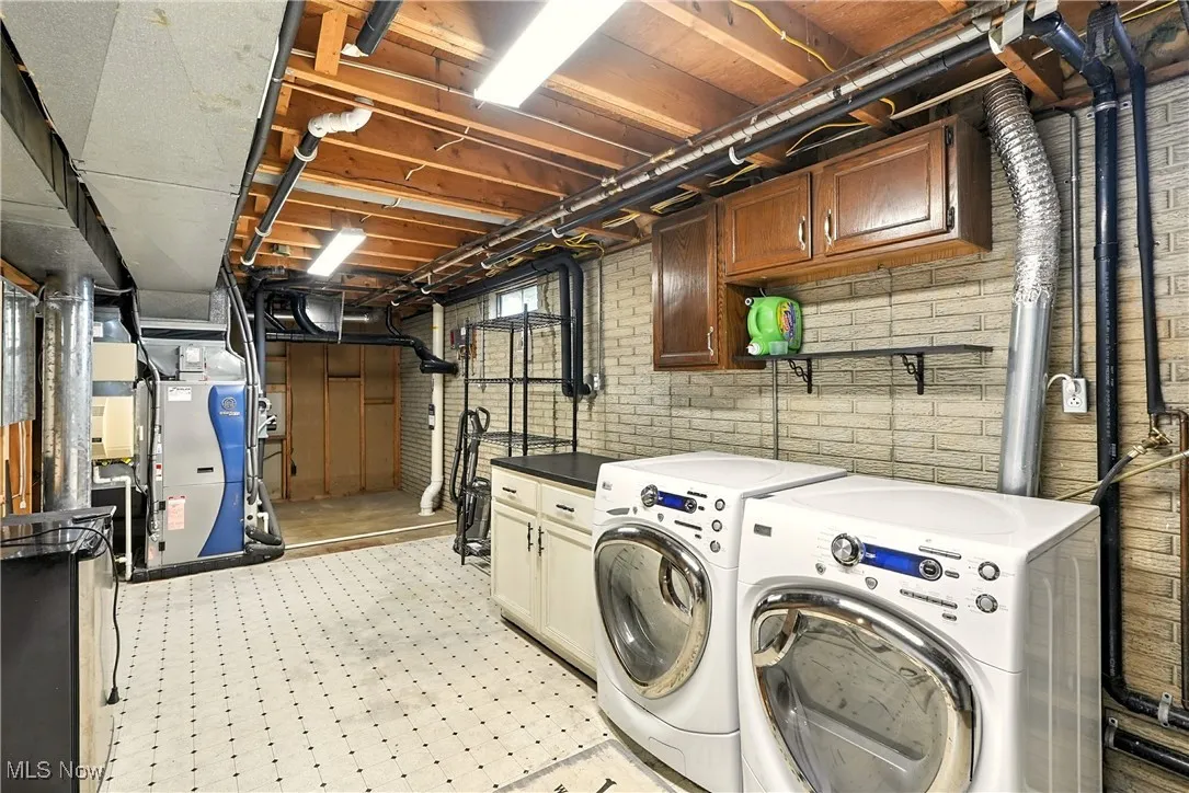 Laundry area featuring cabinet space, light floors, washing machine and clothes dryer, and heating unit
