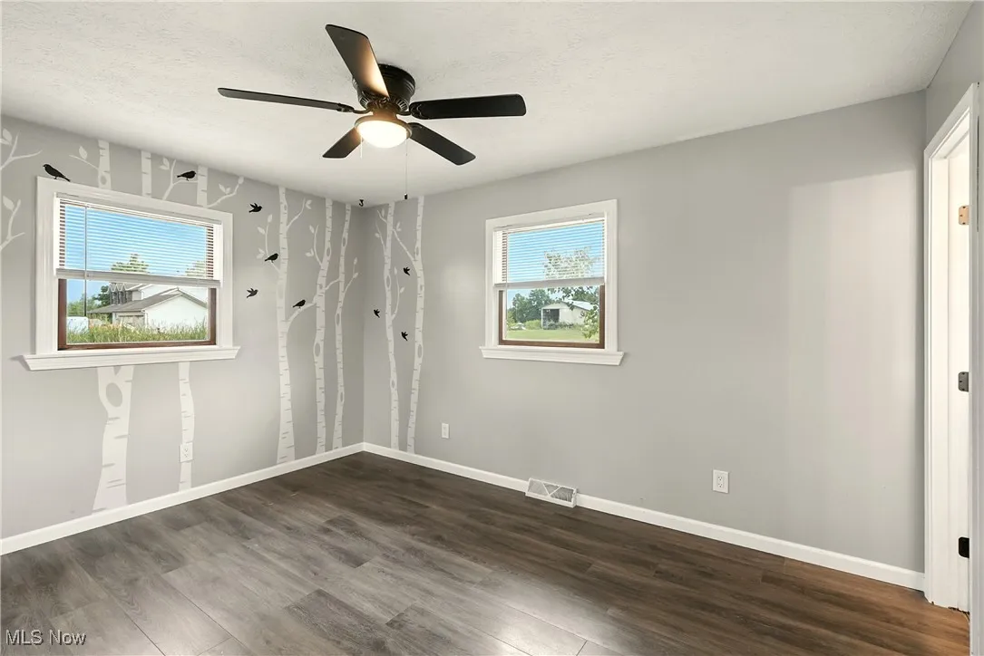 Empty room featuring dark wood finished floors, a textured ceiling, and ceiling fan