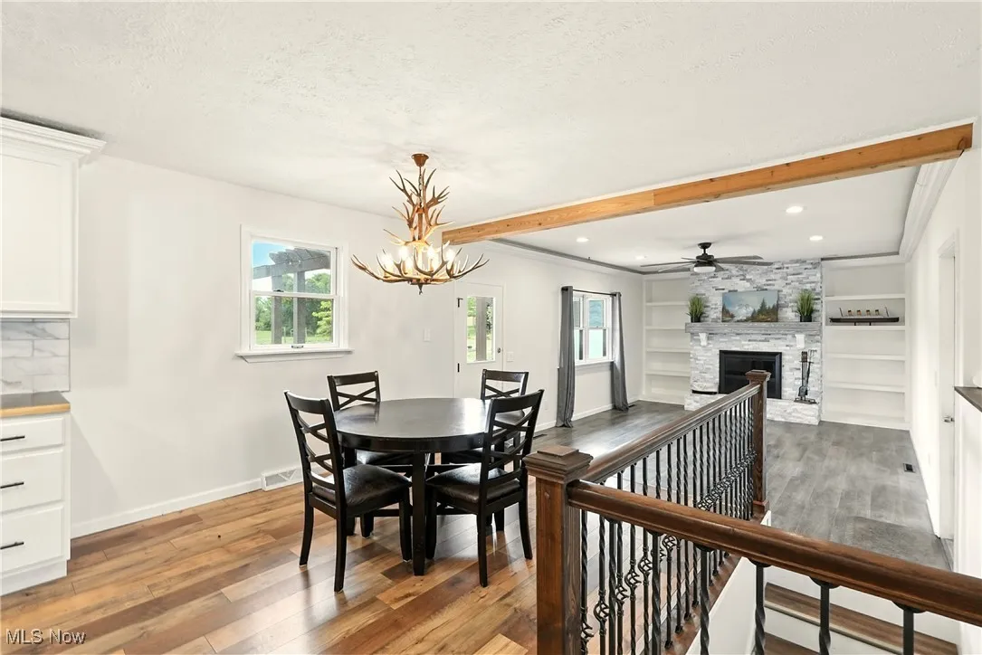 Dining room with light wood finished floors, a fireplace, beamed ceiling, a textured ceiling, and ceiling fan