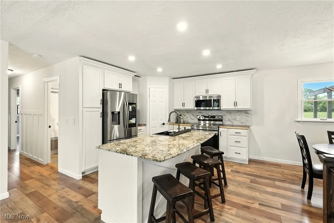 Kitchen featuring stainless steel appliances, white cabinets, a breakfast bar, light wood-type flooring, and a textured ceiling
