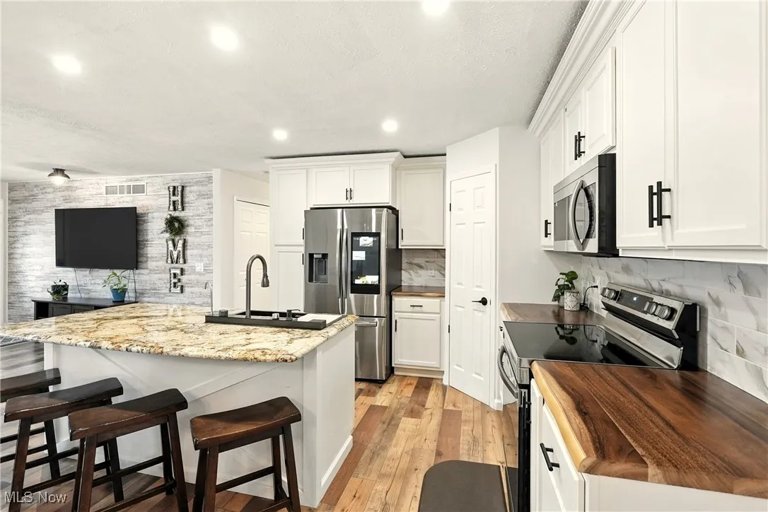 Kitchen featuring stainless steel appliances, a breakfast bar, a kitchen island with sink, light wood-type flooring, and recessed lighting