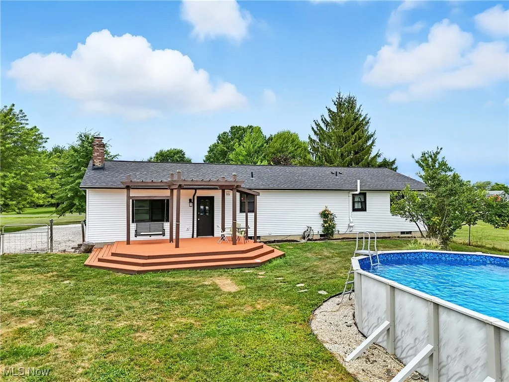 Rear view of property featuring an outdoor pool, a deck, a lawn, and a chimney
