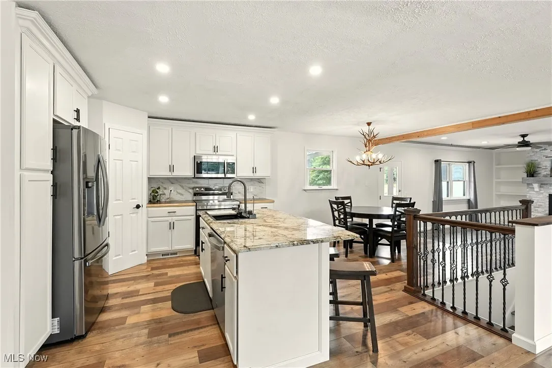Kitchen with stainless steel appliances, recessed lighting, a center island with sink, light wood finished floors, and white cabinetry
