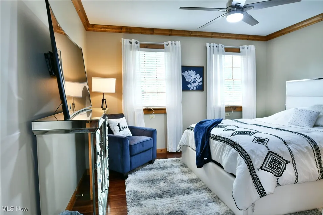Bedroom with dark wood-style floors, ceiling fan, and crown molding