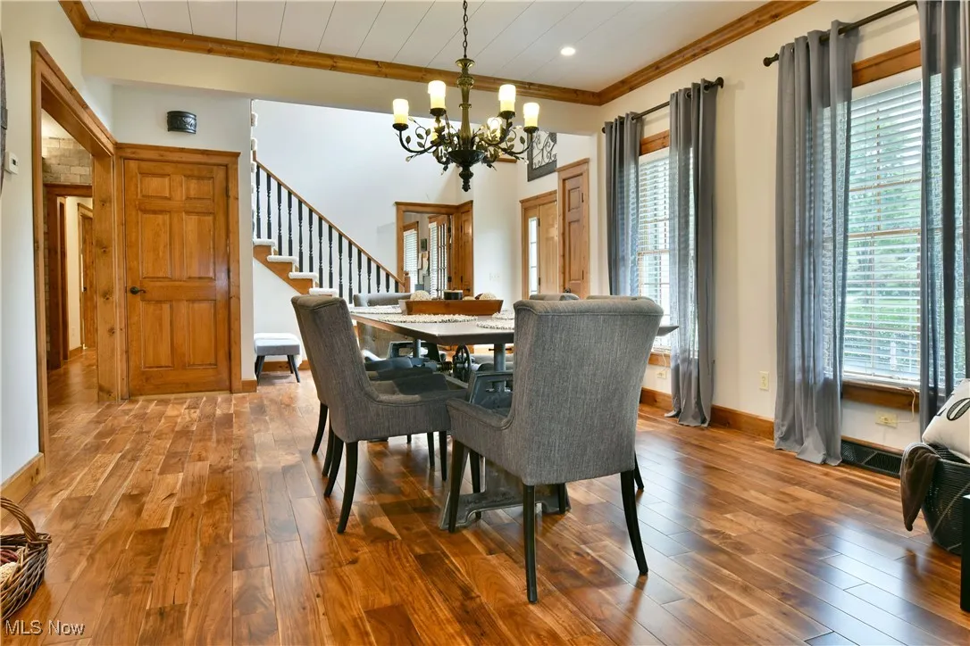 Dining room featuring hardwood / wood-style floors, stairs, crown molding, and a chandelier