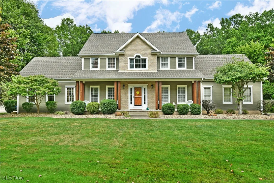 Colonial-style house with roof with shingles, covered porch, and a front lawn