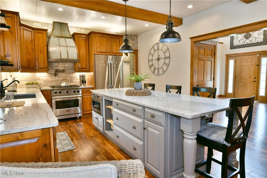 Kitchen featuring light stone countertops, a kitchen bar, tasteful backsplash, premium appliances, and hanging light fixtures