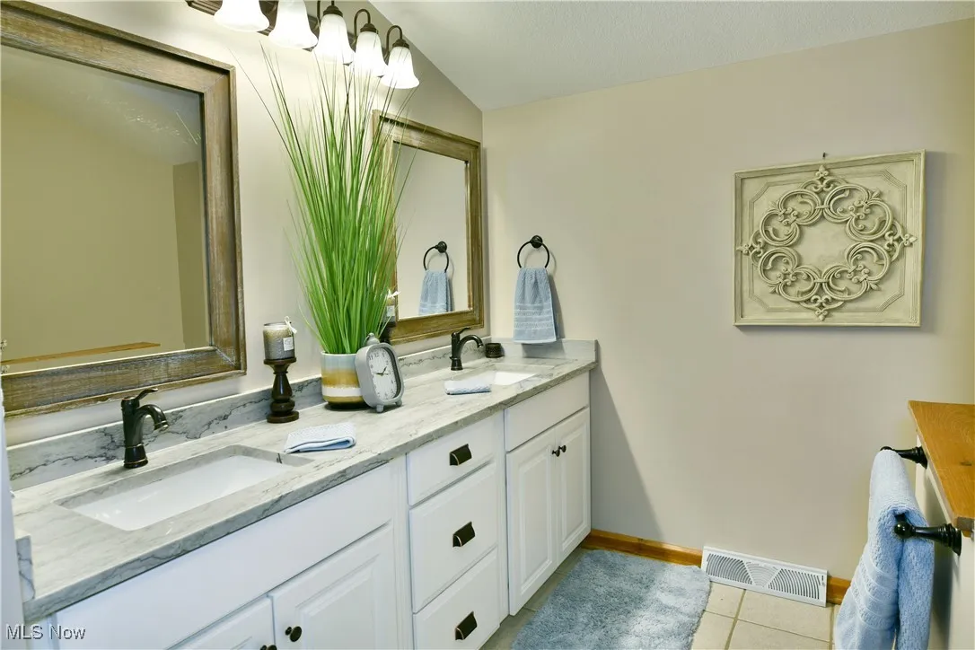 Bathroom featuring double vanity, light tile patterned floors, and vaulted ceiling