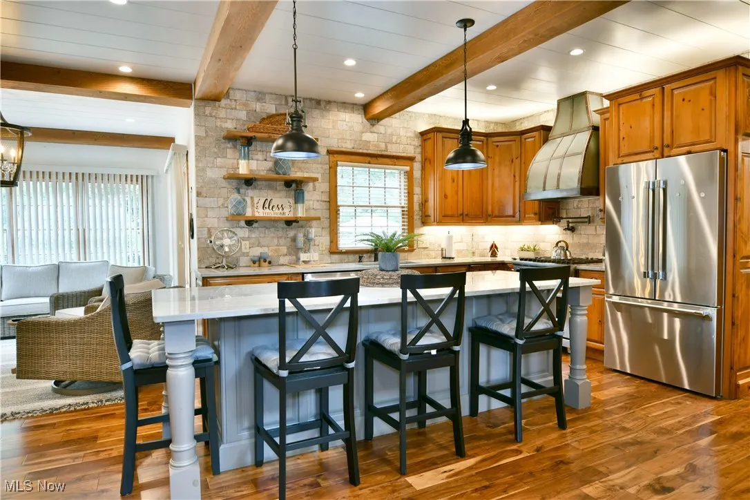 Kitchen with high end refrigerator, beamed ceiling, decorative backsplash, decorative light fixtures, and a kitchen breakfast bar