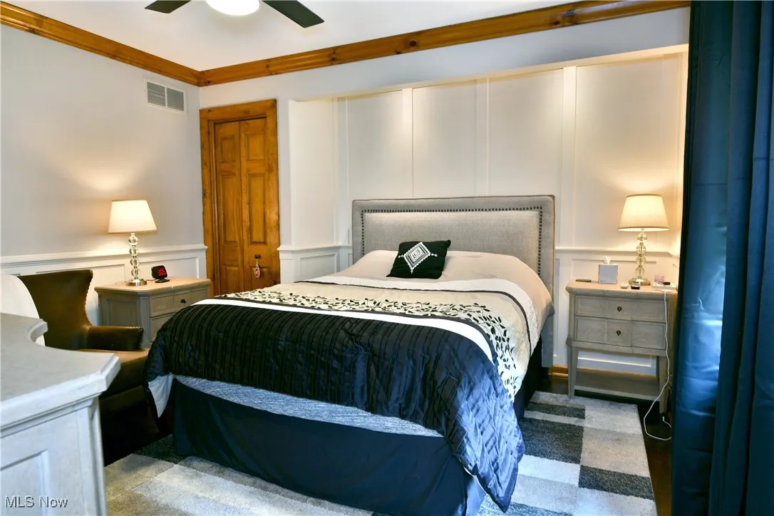 Bedroom featuring a decorative wall, a ceiling fan, wainscoting, and crown molding