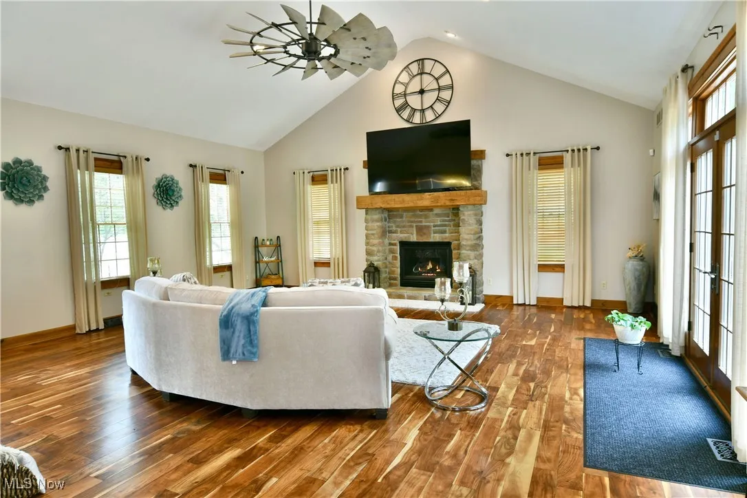Living room featuring a fireplace, plenty of natural light, high vaulted ceiling, wood finished floors, and a ceiling fan