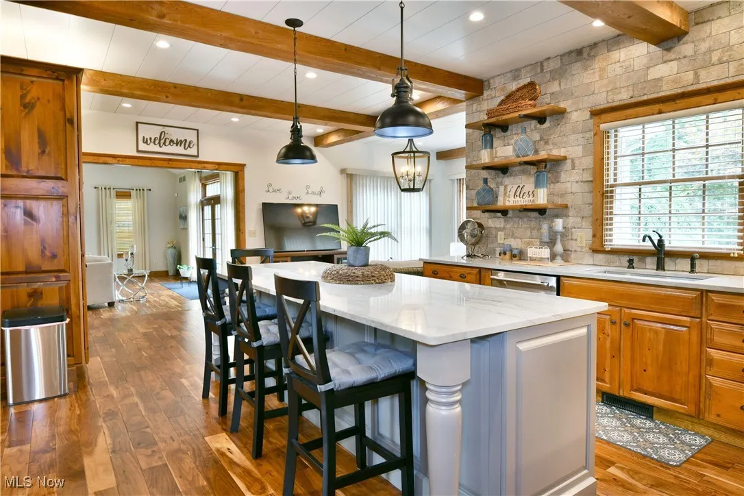 Kitchen with dark wood-type flooring, decorative light fixtures, a breakfast bar, light stone counters, and brown cabinetry