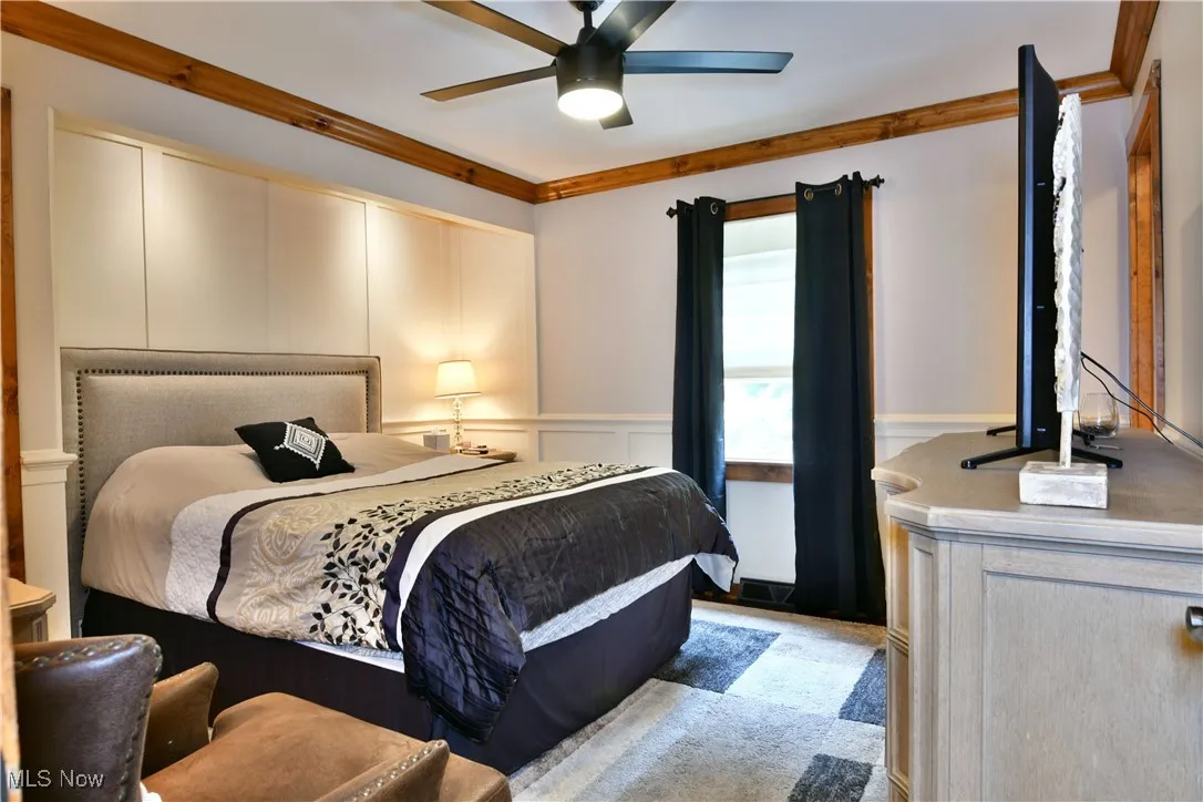 Bedroom with a decorative wall, crown molding, wainscoting, and a ceiling fan