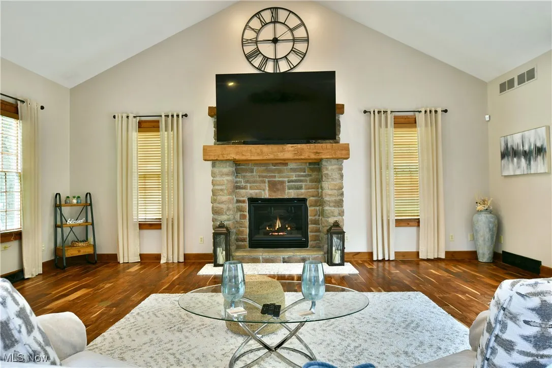 Living area with dark wood-style floors, a glass covered fireplace, and high vaulted ceiling
