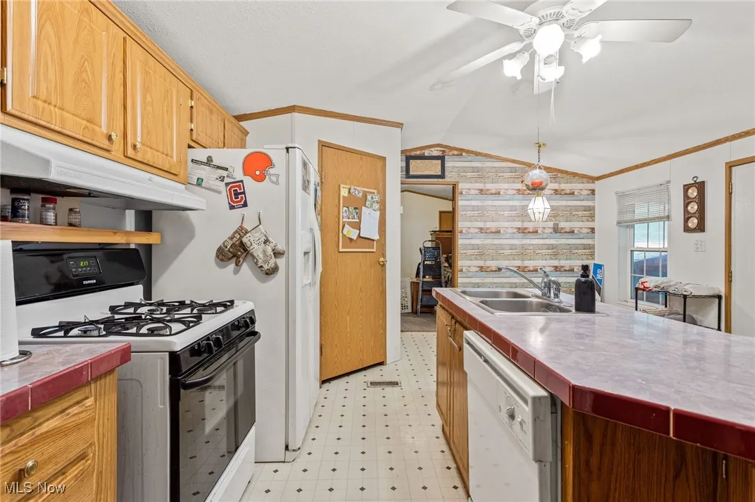 Kitchen with white appliances, tile counters, crown molding, under cabinet range hood, and lofted ceiling