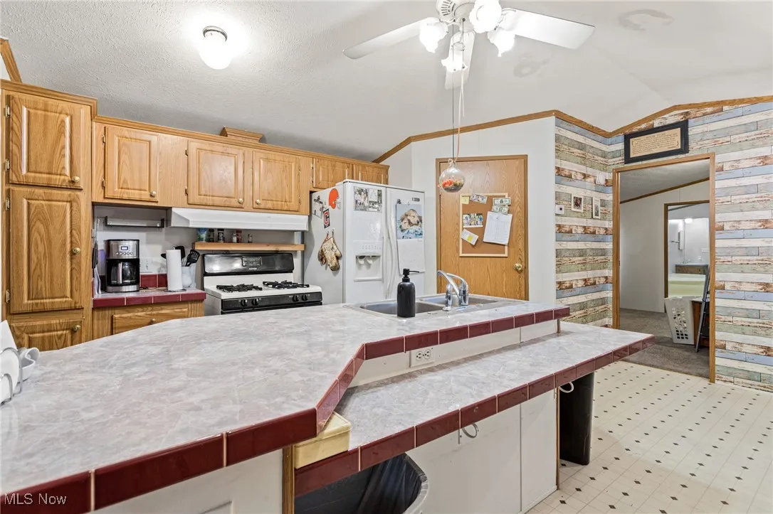 Kitchen with lofted ceiling, white appliances, tile countertops, ornamental molding, and a ceiling fan