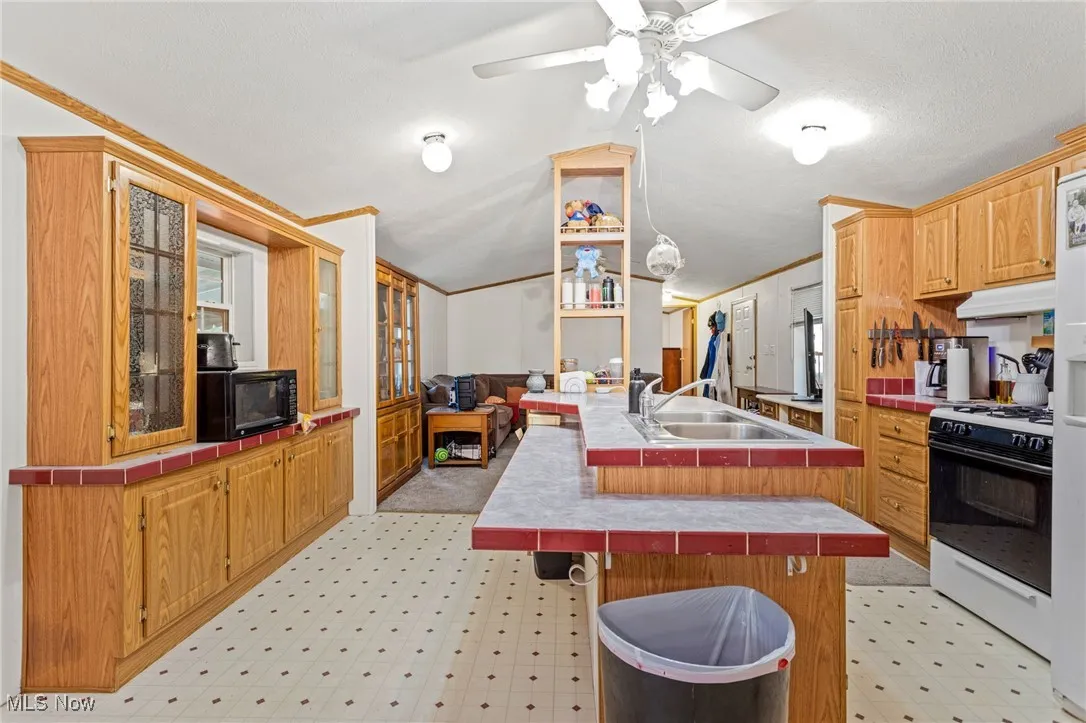 Kitchen with tile countertops, white appliances, lofted ceiling, crown molding, and an island with sink