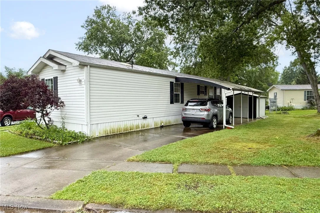 View of front of house with concrete driveway, a carport, and a front lawn