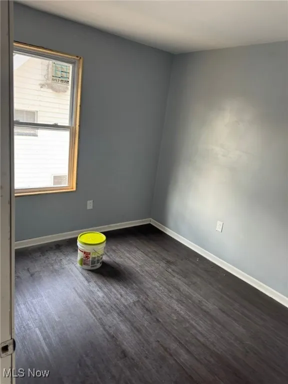 Empty room featuring baseboards and dark wood-style flooring