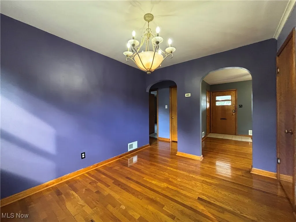 Spare room featuring wood finished floors, a chandelier, and arched walkways