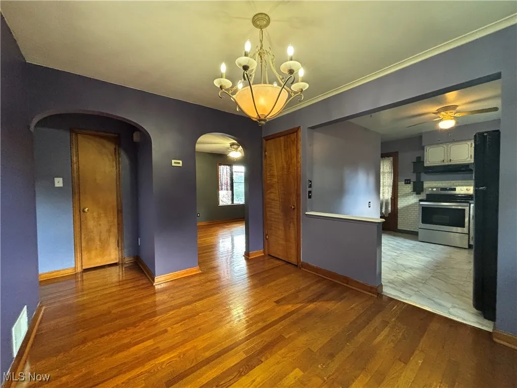 Unfurnished room featuring wood finished floors, arched walkways, a chandelier, and a ceiling fan