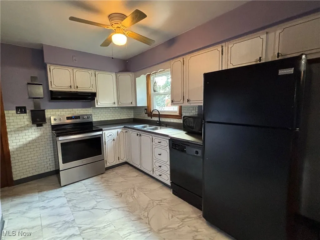 Kitchen featuring black appliances, light marble finish flooring, dark countertops, under cabinet range hood, and ceiling fan