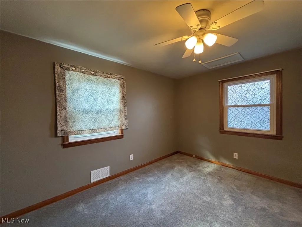 Carpeted empty room with ceiling fan and attic access