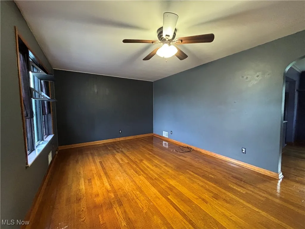 Spare room with arched walkways, wood finished floors, and a ceiling fan