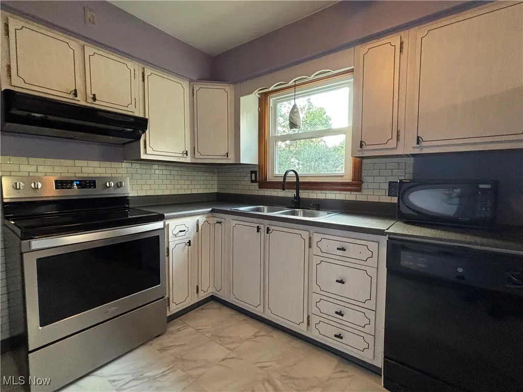 Kitchen featuring black appliances, light marble finish floors, under cabinet range hood, and backsplash