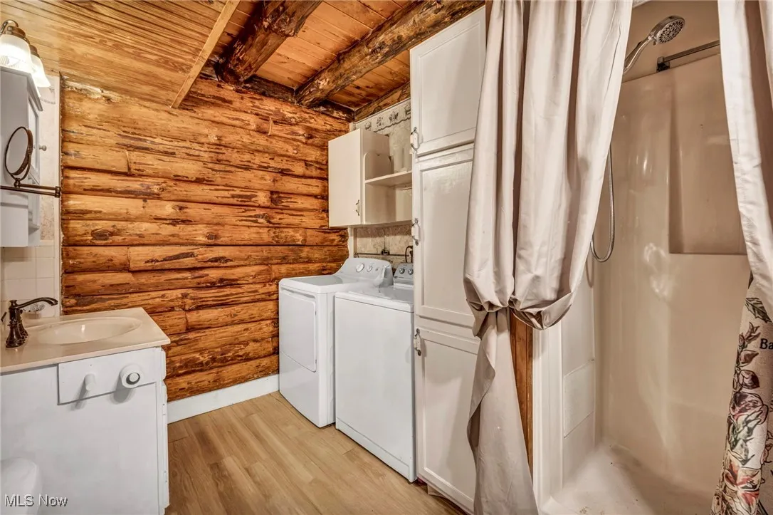 Laundry room featuring rustic walls, laundry area, wooden ceiling, a sink, and washing machine and dryer