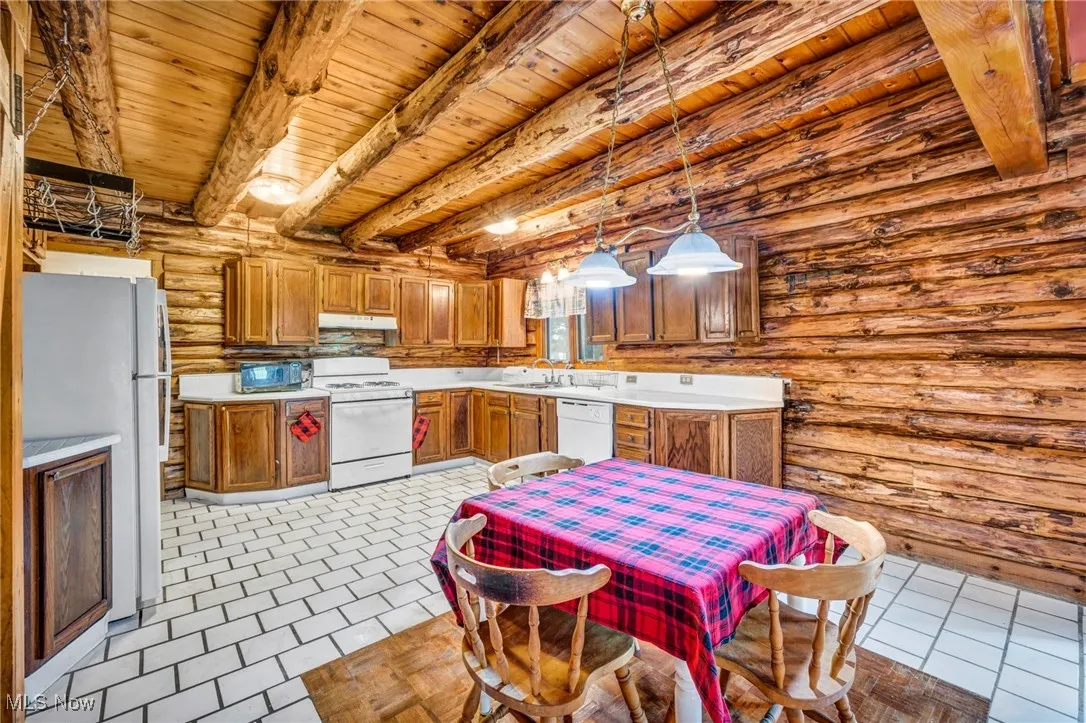 Kitchen with brown cabinets, white appliances, beamed ceiling, wood ceiling, and log walls