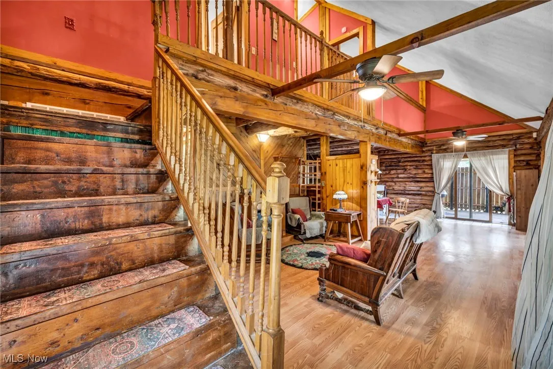 Stairs with beam ceiling, rustic walls, wood finished floors, ceiling fan, and high vaulted ceiling