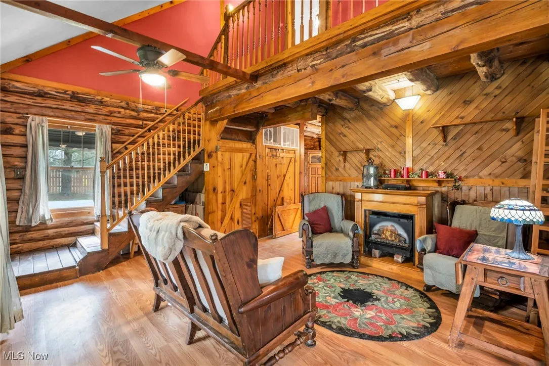 Living room featuring wood finished floors, a ceiling fan, vaulted ceiling with beams, and stairway