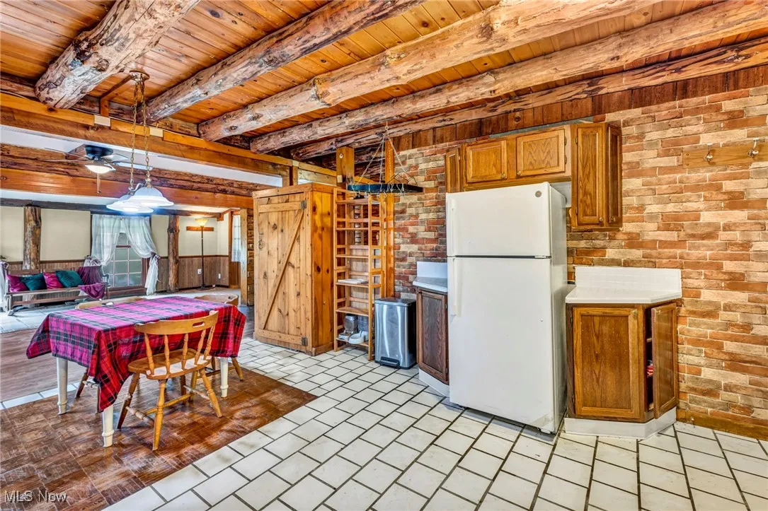 Kitchen with light countertops, wooden ceiling, beamed ceiling, freestanding refrigerator, and brick wall