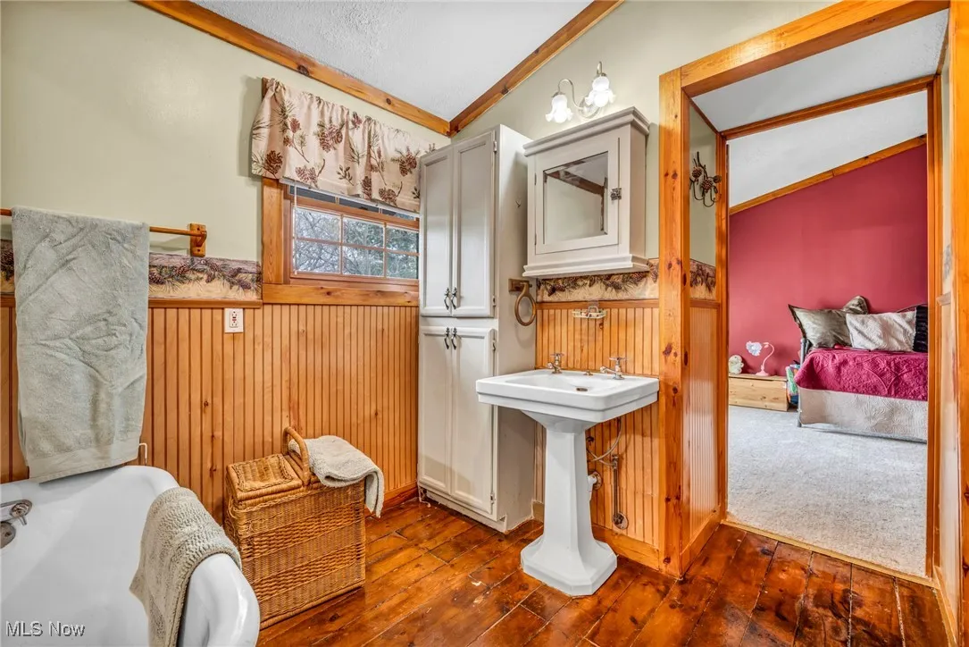 Bathroom with wainscoting, vaulted ceiling, an inviting chandelier, crown molding, and wood-type flooring
