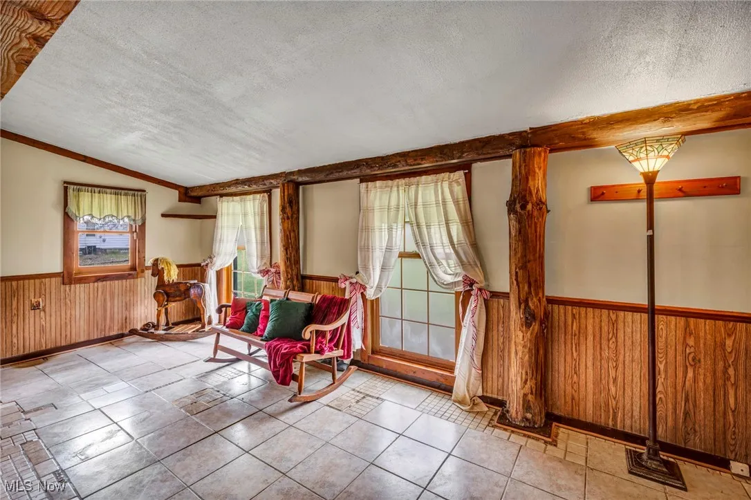 Living area featuring lofted ceiling, a wainscoted wall, wood walls, and a textured ceiling