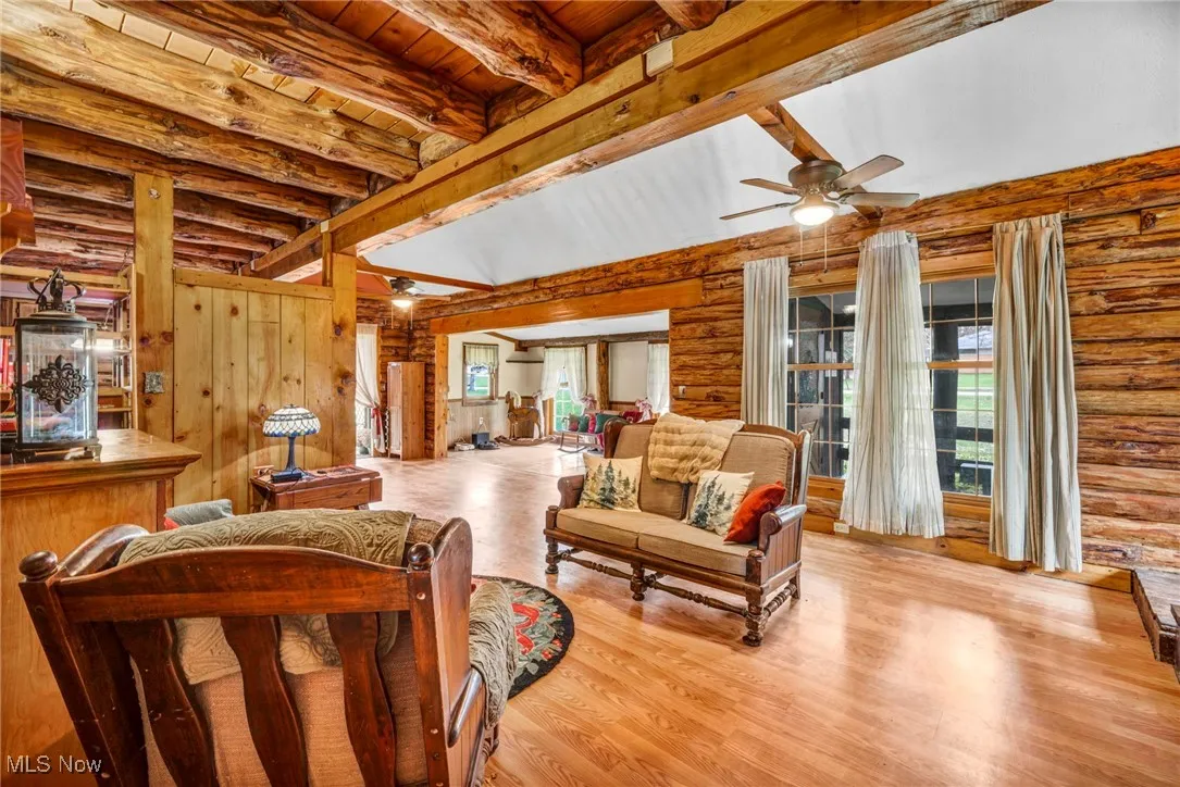 Living room with beam ceiling, log walls, wood finished floors, ceiling fan, and wood ceiling