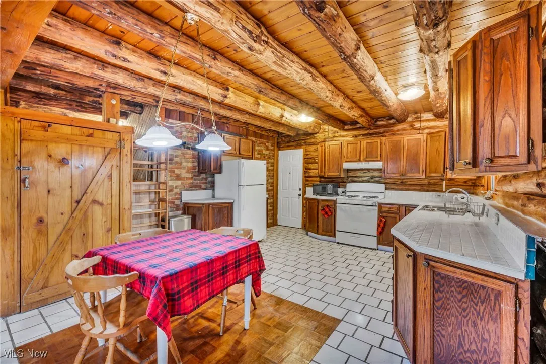 Kitchen featuring under cabinet range hood, light countertops, a sink, white appliances, and wood ceiling