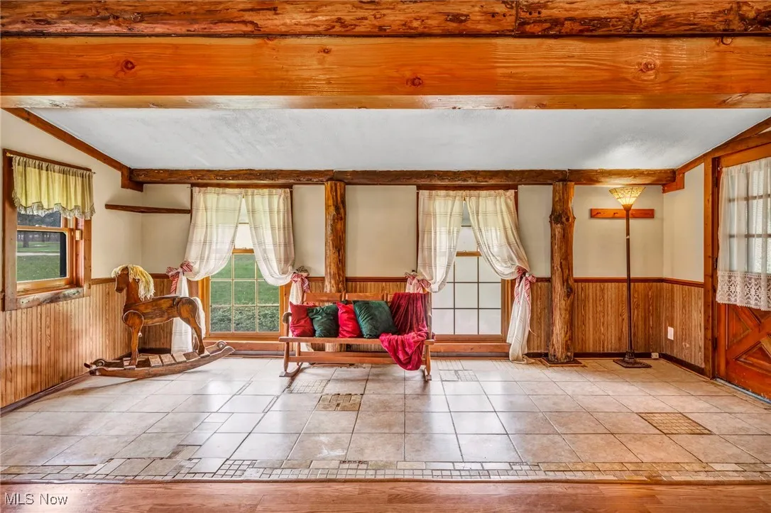 Living area featuring wood walls, a wainscoted wall, and vaulted ceiling with beams