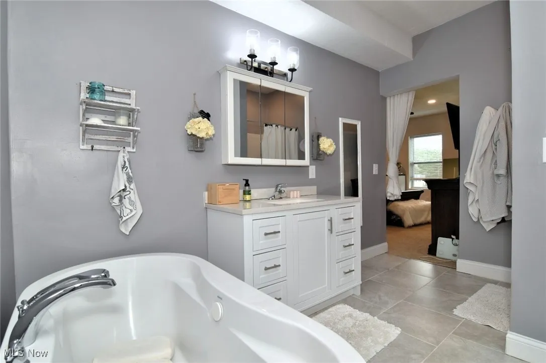 Full bathroom with vanity, a freestanding tub, ensuite bath, light tile patterned floors, and recessed lighting