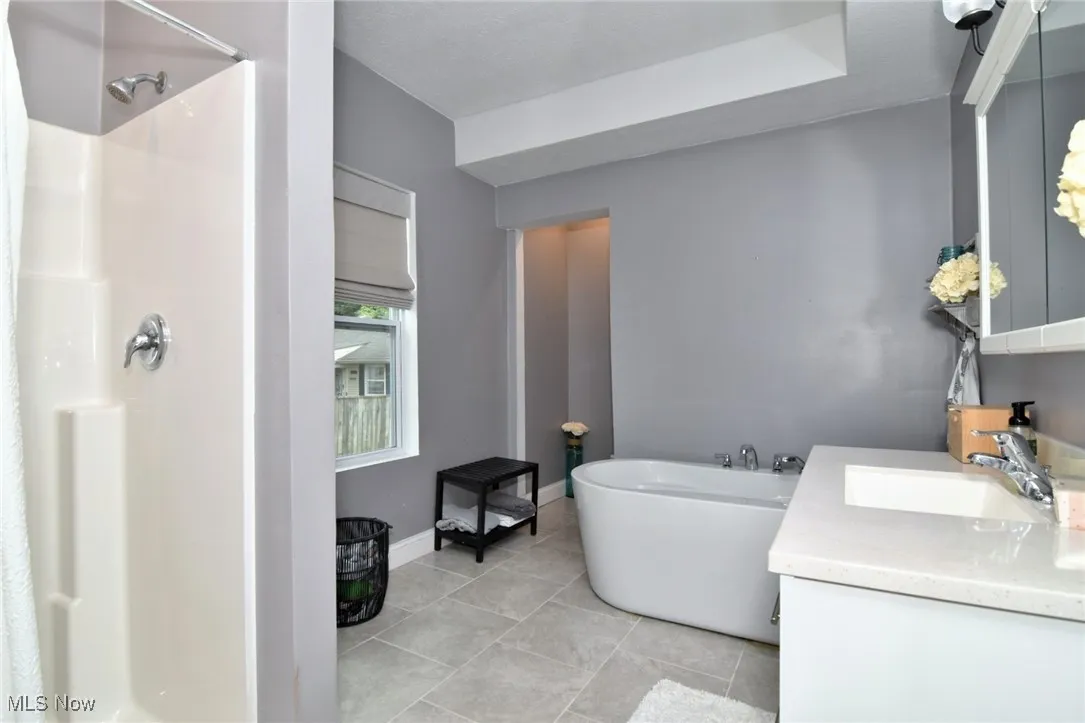 Full bath featuring a freestanding bath, a stall shower, vanity, and light tile patterned flooring