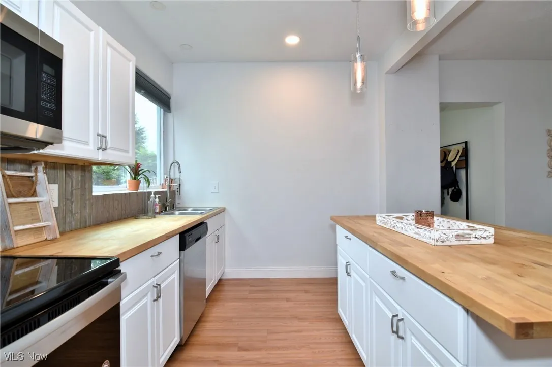 Kitchen with wooden counters, white cabinets, stainless steel appliances, decorative light fixtures, and light wood finished floors