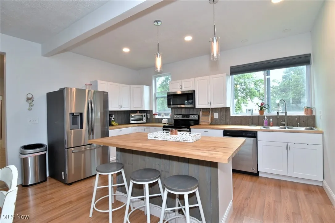 Kitchen featuring tasteful backsplash, decorative light fixtures, appliances with stainless steel finishes, wooden counters, and beamed ceiling