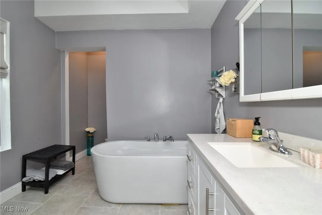 Full bath featuring vanity, a soaking tub, and light tile patterned floors