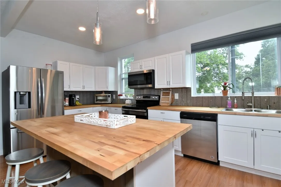 Kitchen featuring decorative backsplash, appliances with stainless steel finishes, white cabinets, light wood-style floors, and a kitchen bar