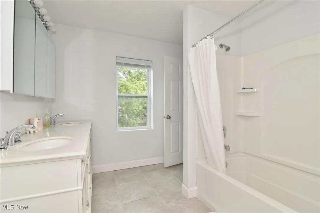 Full bathroom with shower / bathtub combination with curtain, double vanity, and light tile patterned floors