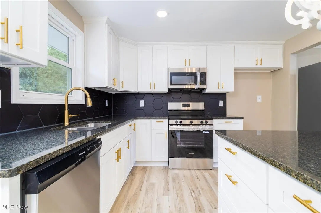 Kitchen featuring appliances with stainless steel finishes, white cabinetry, dark stone counters, light wood finished floors, and recessed lighting