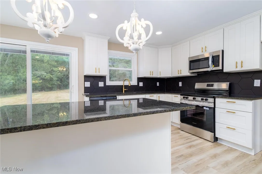 Kitchen featuring stainless steel appliances, tasteful backsplash, dark stone counters, decorative light fixtures, and white cabinets