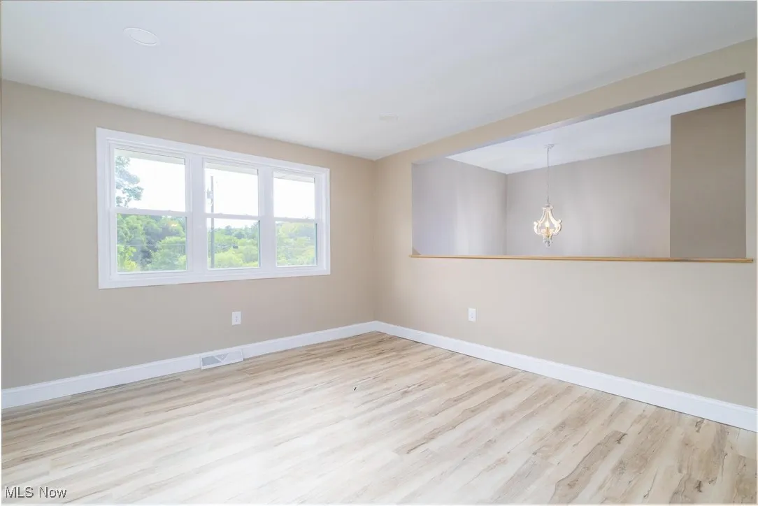 Unfurnished room with light wood-type flooring and a chandelier